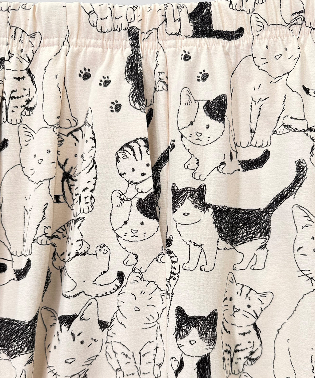 クニオコレクション(KUNIO COLLECTION)のチアフルカーブパンツ(アイボリー)。ミルクティ地にしなやかな線画で描かれたネコちゃん柄が爽やかで遊び心溢れるデザイン。脇線の柔らかなカーブと2本のタックでお腹周りをすっきり見せるシルエットが特徴で、しなやかなストレッチ素材による快適な履き心地のスタイルアップボトムス。