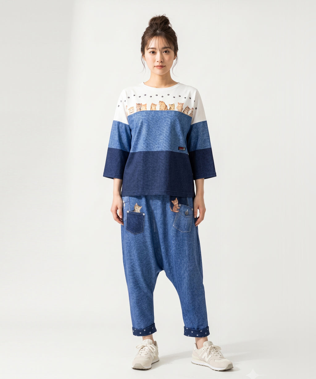 クニオコレクション(KUNIO COLLECTION)のスリーステップ(ネコ)ドルマンTシャツ。バイカラーデニム風のデザインに愛らしいネコちゃん柄をあしらった、ゆるっとオフボディなシルエットの一枚。さらりとした軽い着心地と心地よいストレッチ素材が特徴のトップス。