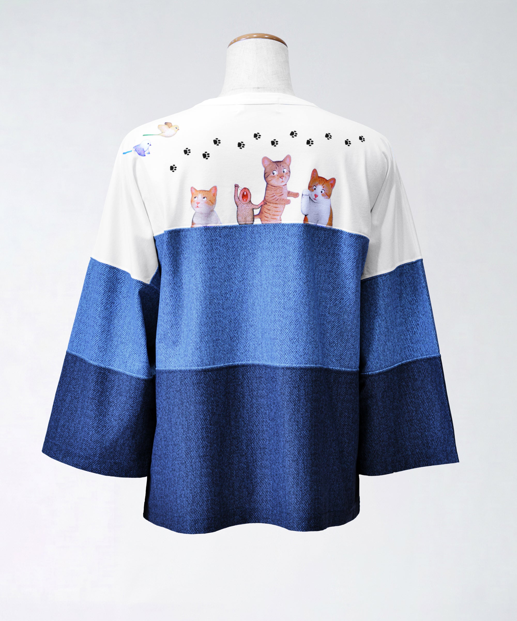 クニオコレクション(KUNIO COLLECTION)のスリーステップ(ネコ)ドルマンTシャツ。バイカラーデニム風のデザインに愛らしいネコちゃん柄をあしらった、ゆるっとオフボディなシルエットの一枚。さらりとした軽い着心地と心地よいストレッチ素材が特徴のトップス。