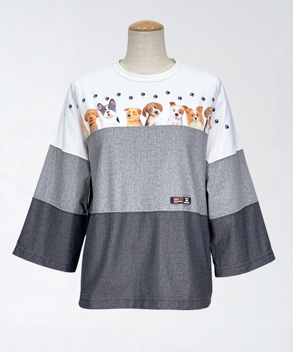 クニオコレクション(KUNIO COLLECTION)のスリーステップ(イヌ)ドルマンTシャツ。バイカラーのブラックデニム風デザインに愛らしいワンちゃん柄をあしらった、ゆるっとオフボディなシルエットの一枚。さらりとした軽い着心地と心地よいストレッチ素材が特徴のトップス。