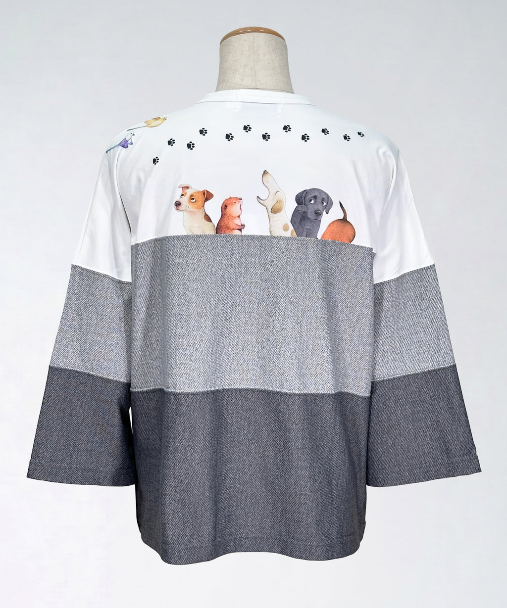 クニオコレクション(KUNIO COLLECTION)のスリーステップ(イヌ)ドルマンTシャツ。バイカラーのブラックデニム風デザインに愛らしいワンちゃん柄をあしらった、ゆるっとオフボディなシルエットの一枚。さらりとした軽い着心地と心地よいストレッチ素材が特徴のトップス。